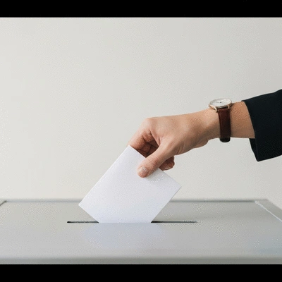 Hand placing a ballot into a ballot box, emphasizing civic engagement